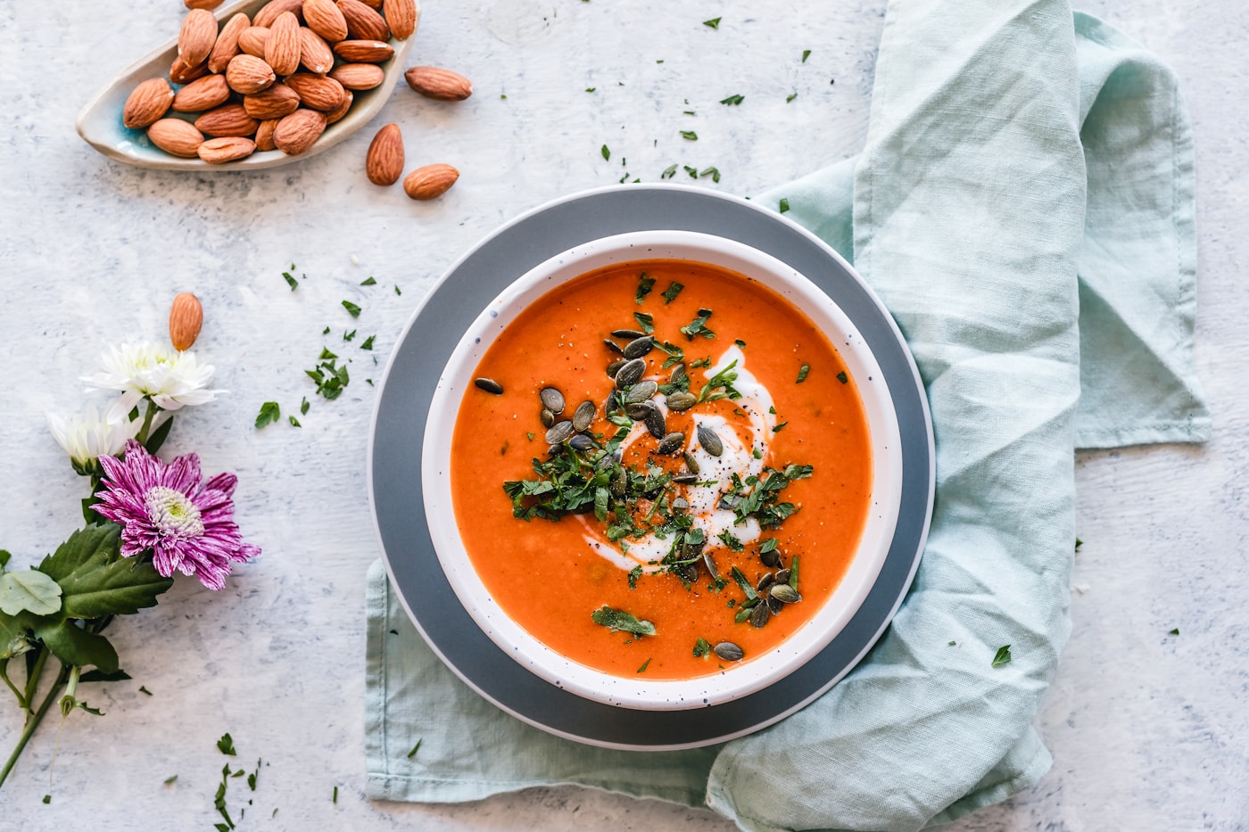 A bowl of orange-red soup with a swirl of cream, herbs, and pumpkin seeds.
